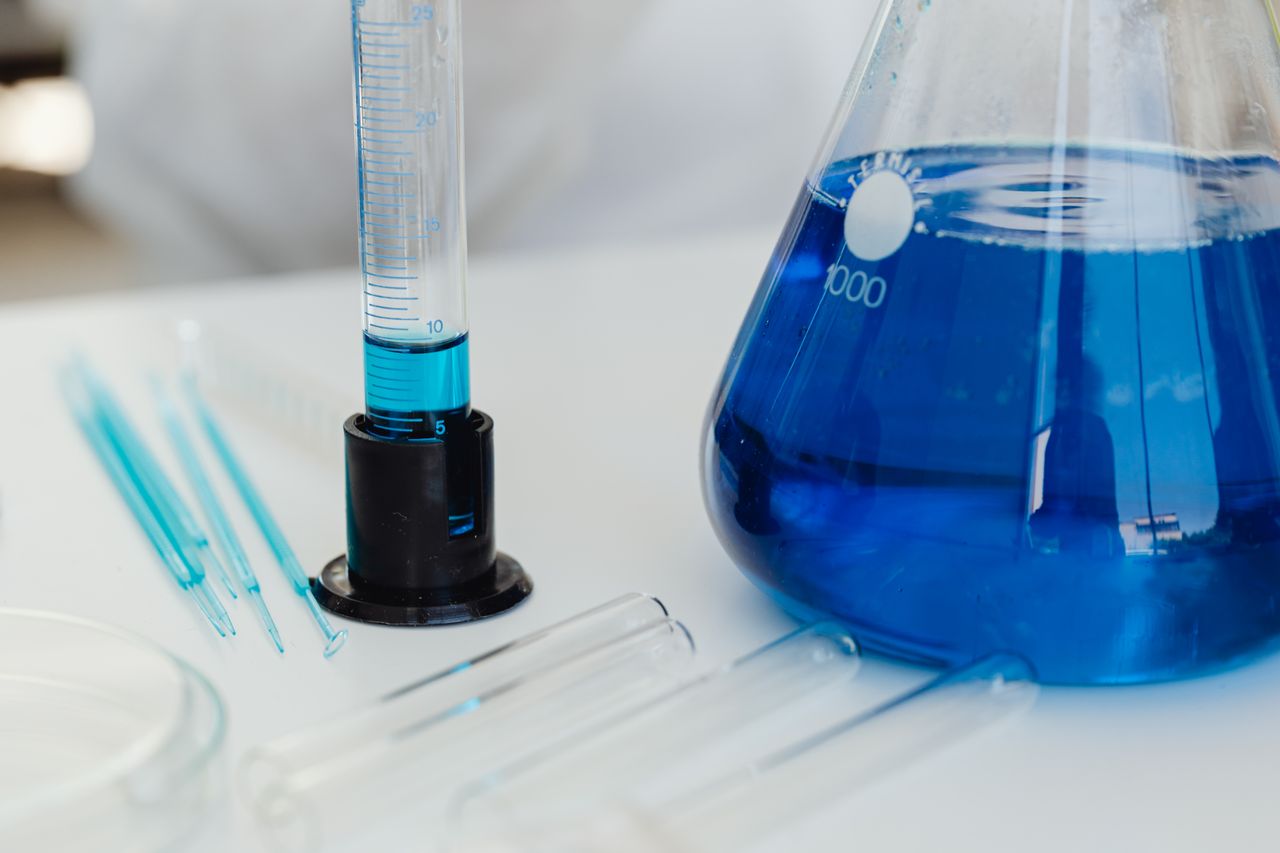 Menu Detailed close-up of laboratory equipment including test tubes and Erlenmeyer flask with blue liquid.