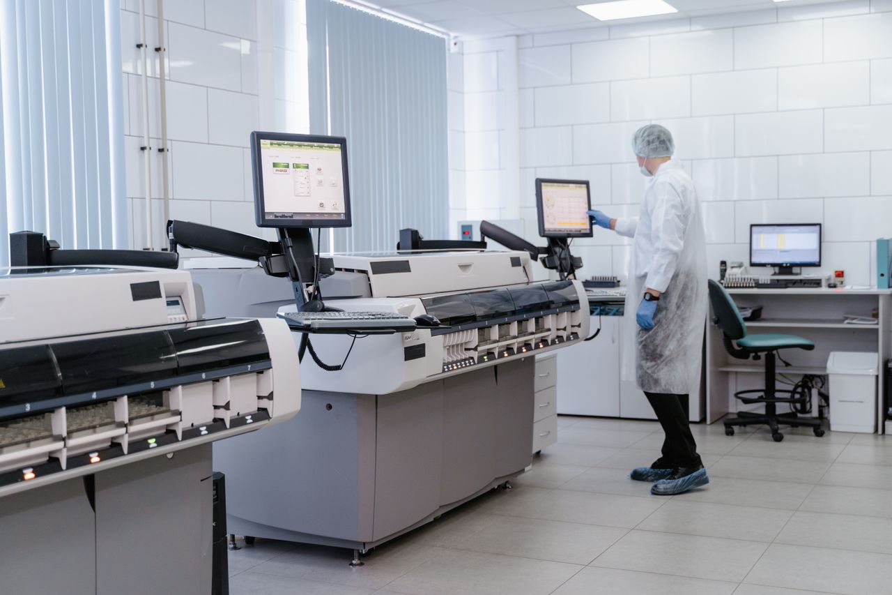 menu-01 Scientist in a lab gown interacting with equipment in a modern laboratory setting.